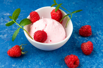 Raspberry ice cream in a white cup with fresh raspberries and a sprig of mint on a blue background. A romantic and delicious dessert. Close-up