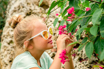 A cute curious little girl in yellow sunglasses smiling and looking at exotic flowers