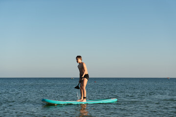A 12 year old boy learns to stand on a SUP board in the sea near the shore.