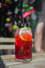Cold berry lemonade with ice, mind and lemon on table against the summer outdoor cafe