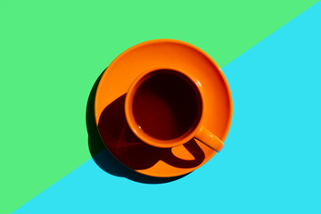 top view of orange cup saucer with black tea or coffee on the colour background with green and blue. copy space.