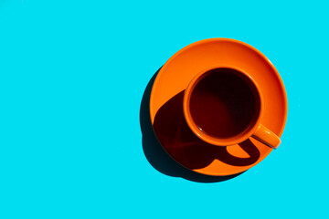 top view of orange cup and saucer with black tea or coffee on the blue background. copy space.