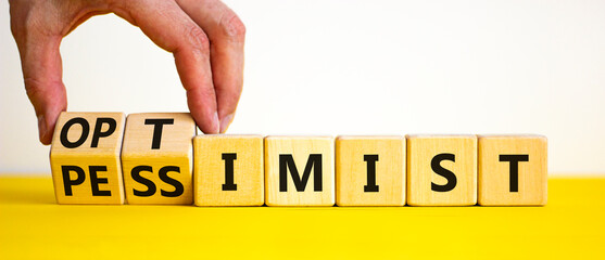 Pessimist or optimist symbol. Businessman turns cubes and changes the word 'pessimist' to 'optimist'. Beautiful yellow table, white background. Business, optimist or pessimist concept. Copy space.