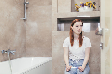 young frustrated woman looking at a quick positive or negative result pregnancy test sitting in...