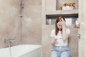 young frustrated woman looking at a quick positive or negative result pregnancy test sitting in...