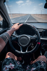 A person driving on the highway with a tattoo on his arm, sneakers and shorts with a flower design and a sky with white clouds.