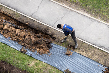 Migrant labor. A worker digging a ditch along a pavement in summer.