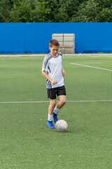 The boy loves to play football, trains with the ball on the artificial turf and scores a goal. The boy plays football