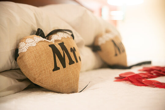 Beige Mr. & Mrs. Heart pillows with white lace and black letters on a bed