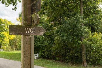 Wooden direction sign to the public toilet in the outdoor green garden park