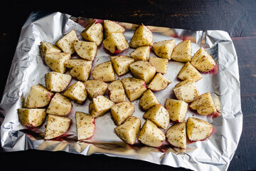 Raw Seasoned Potatoes on a Foil Lined Sheet Pan: Uncooked red potatoes coated in olive oil, spices,...