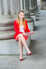 Dressing in a red blazer, white under wear, a red skirt and open toes high heels, crossing legs, a female college student is sitting by columns on campus, studying on a tablet computer..