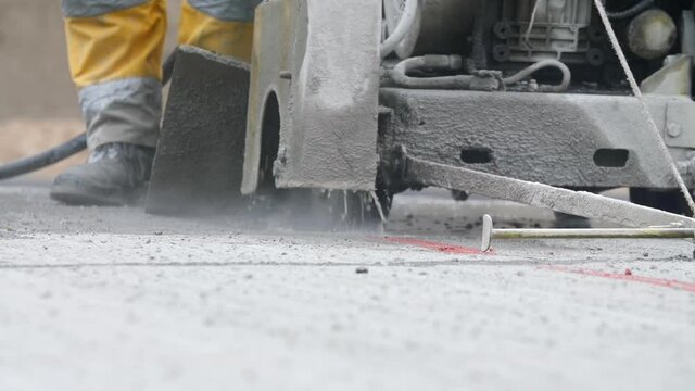 Close-up view of feet of highway road worker in uniform cutting asphalt or blacktop using concrete saw or cutter machine. Concept of electric tool for roadway pavement removal, motorway maintenance.