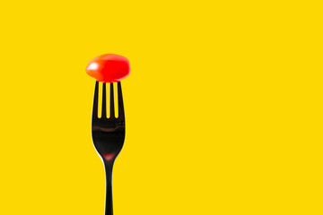 Fork with tomato on yellow background, copy space for text 