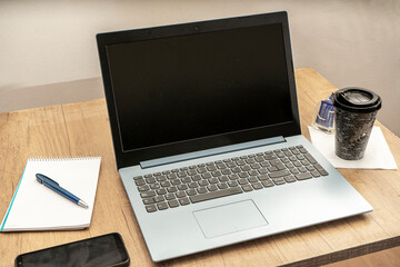 Snapped view of a desk with an open laptop, a notepad, a glass of coffee, and a cell phone ready to work from home. Technology concept.