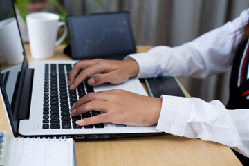 Fototapeta premium Young woman sitting, using laptop, tablet, notebook and calculator working from home. Closeup shot of unrecognizable woman, hands working on computer keyboard. 