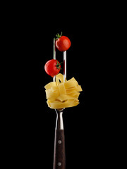 Raw fettuccine pasta with cherry tomatoes on a two-pronged fork. Black background.