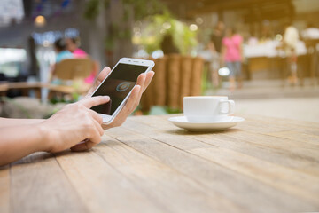 Closeup image of hands woman playing mobile phone. With a cup of coffee near On a wooden table in a coffee shop