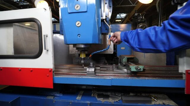 Worker in blue uniform adjusts cooling pipe on drilling machine tool in light workshop of contemporary plant closeup