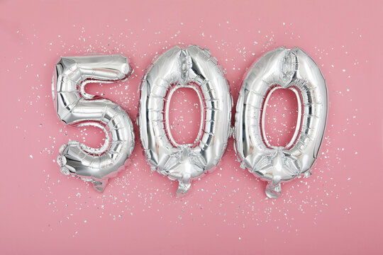 From above of silver shiny balloons demonstrating number 500 on pink background with scattered glitter