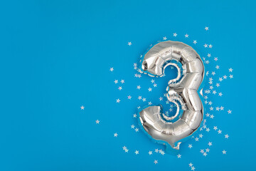Silver balloon 3 on a blue background with confetti stars. Number three 3. Holiday Party Decoration...