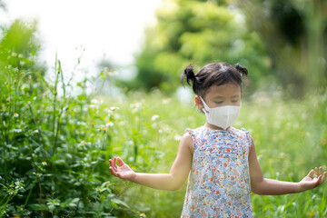 Adorable small girl with protective face mask standing at field.