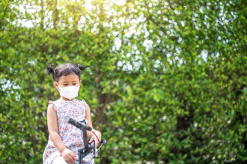 Cute small girl with protective face mask on bicycle outdoor.