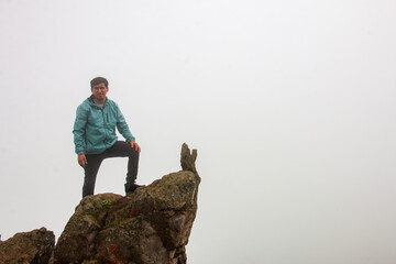 Man standing on top of a rocky summit. background a sky of clouds and mist.