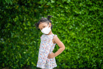 Obraz premium Adorable small girl with healthy face mask standing against green nature background.