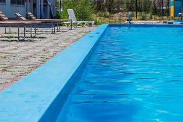 Outdoor swimming pool with a clear blue water. Steel railings stairs and sun loungers.