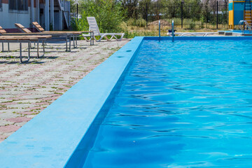 Outdoor swimming pool with a clear blue water. Steel railings stairs and sun loungers.
