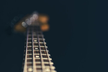 Close-up of a bass guitar fretboard on a blurred dark background.