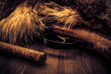 Hunting rifle with cuban cigar lying next to the animal's fur produced. View close-up