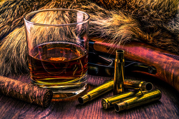 Hunting rifle with glass of whiskey and cuban cigar lying next to the animal's fur produced. View...