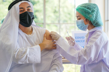 Portrait of Arab Muslim man looking at while getting covid vaccine in clinic or hospital, with hand...