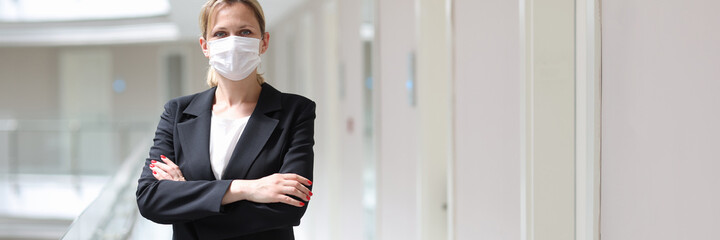Businesswoman in medical protective mask stands with folded arms in hotel corridor