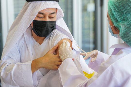 woman Nurse preparing injecting vaccine to shoulder of Arab Muslim man in clinic or hospital for getting immunity to protect virus. people wearing protective mask.