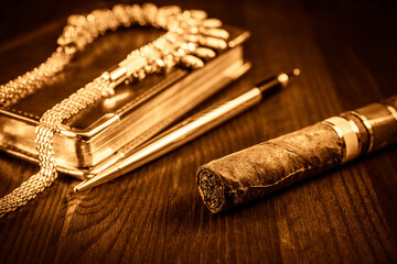 Golden pen with a leather diary and cuban cigar with jewellery on a mahogany table