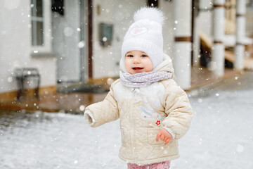 Happy little baby girl making first steps outdoors in winter through snow. Cute toddler learning walking. Child having fun on cold snowy day. Baby's first snow, activity. Winter walk outdoors
