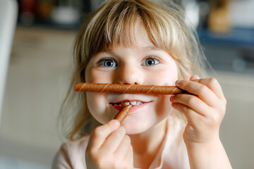 Portrait of happy little preschool girl holding chocolate waffle rolls. Smiling hungry toddler...