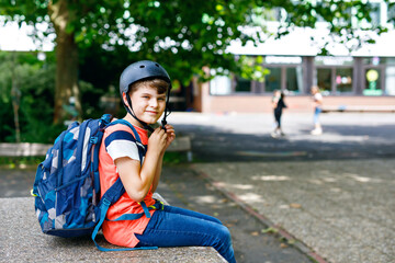 Happy little kid boy with satchel and bicycle helmet. Schoolkid on the way to middle or high...
