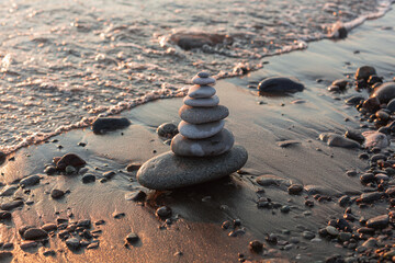Pyramid of stones on the beach at sunset, beautiful seascape, rest and seaside vacation concept. 
