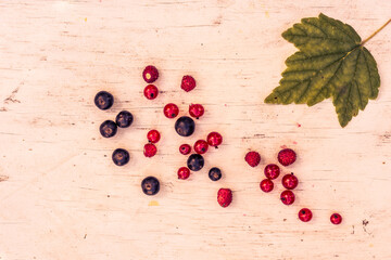 Berries red and black currants with strawberry are scattered on the old wooden table