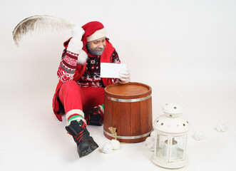 Santa Claus is sitting on the floor and writing a letter with a pen.