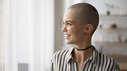 Happy young bald woman with stylish accessories looking in distance, visualizing interesting...