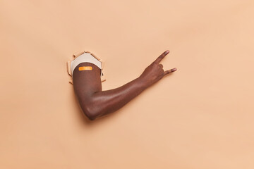 Photo of faceless dark skinned man makes rock n roll hand gesture breaks through beige paper...