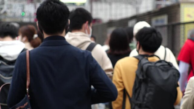 OSAKA, JAPAN - APR 2021 : Back shot of crowd of people walking down the street. View of many commuters after work near the station. Slow motion shot. Japanese city lifestyle concept.