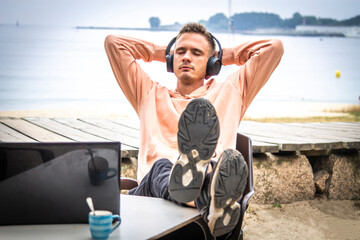relaxed young man with headphones and laptop outdoors