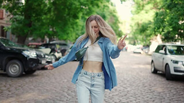 Young stylish woman walking in city street by paved road in dance