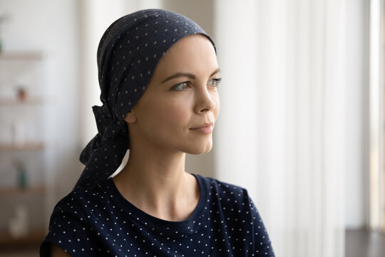 Pensive young caucasian woman wearing scarf on hairless after chemotherapy head looking in distance, visualizing healthy future feeling healthy, thinking of remission or difficult cancer treatment.